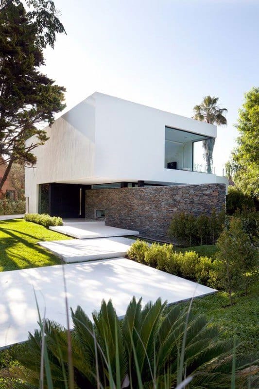 Modern home with white facade, stone accents, sleek pathways, and lush green landscaping.
