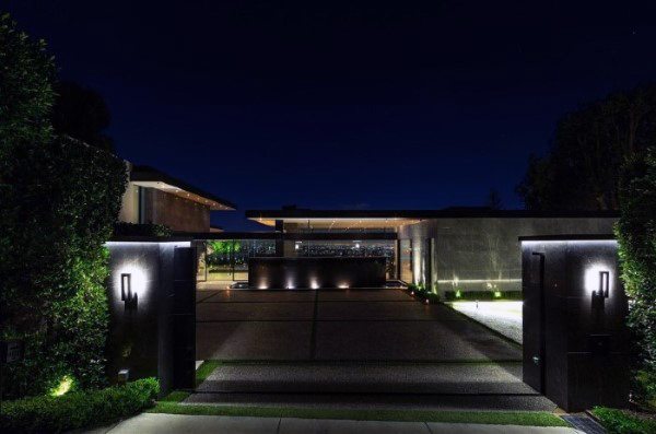 Modern luxury home entrance at night with illuminated driveway and sleek gate design.