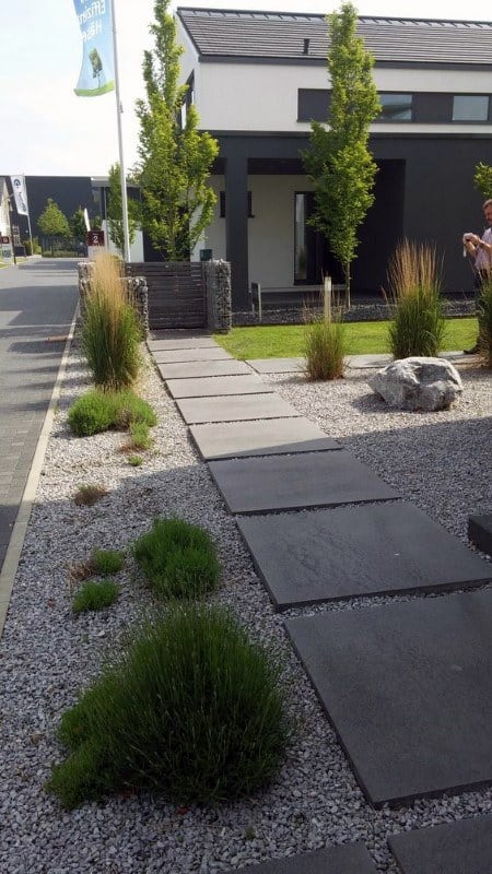 Contemporary walkway with large slate pavers, gravel, ornamental grasses, and a modern facade.