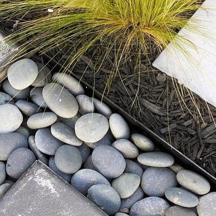 Close-up of modern landscaping with smooth gray pebbles, ornamental grass, and black mulch.