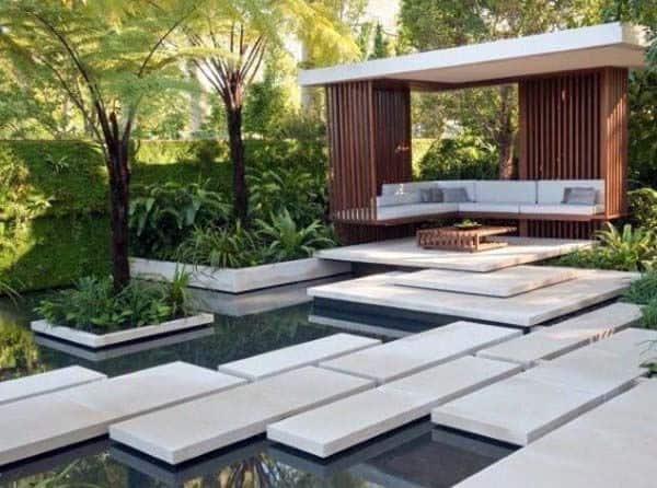 Modern garden with floating concrete steps, lush greenery, and a sleek wooden seating pavilion.