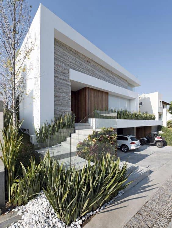 Modern home with clean lines, large windows, lush greenery, and a sleek concrete driveway.