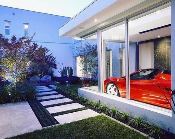 Luxury home with sleek landscaping, glass garage, and red sports car displayed inside.