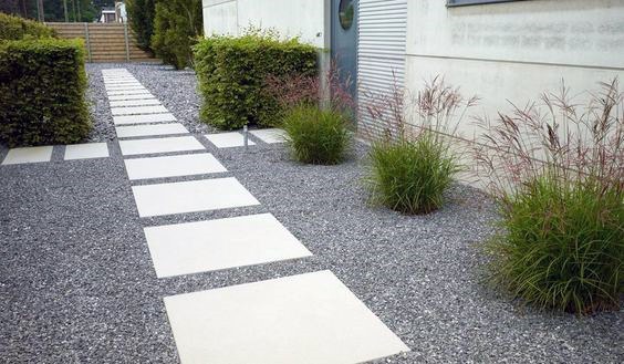 Contemporary pathway with white pavers, gravel, ornamental grasses, and trimmed hedges.