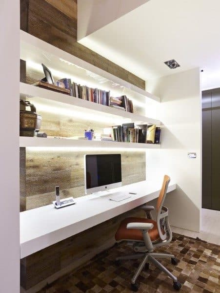 Modern home office with built-in desk, wooden accents, white shelves, a computer, books, and an ergonomic chair