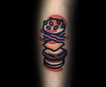 Tattoo of a stylized cheeseburger with a bun, patty, cheese, and toppings on an arm