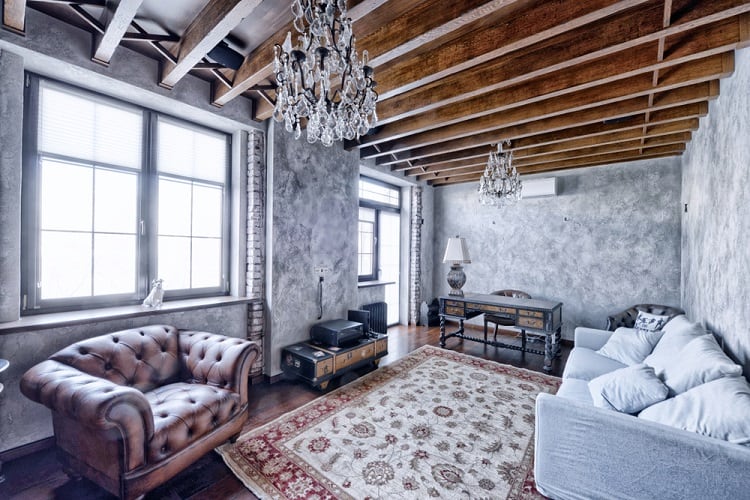 Cozy living room with leather armchair, gray sofa, wooden ceiling beams, chandeliers, and a large ceiling window