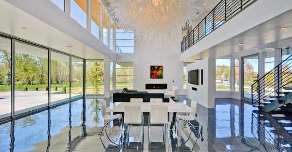 Modern open-concept living space with concrete floors, large windows, sleek furniture, and a unique chandelier