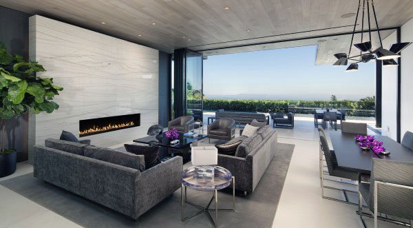 Modern living room with gray sofas, a fireplace, and glass walls opening to a patio with a stunning view
