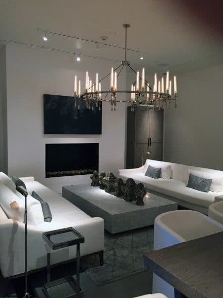 Sleek living room with white sofas, a large gray coffee table, chandelier, and wall-mounted TV