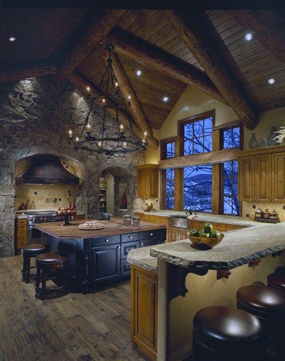 Rustic log cabin kitchen with stone walls, vaulted ceiling, and a large central island.