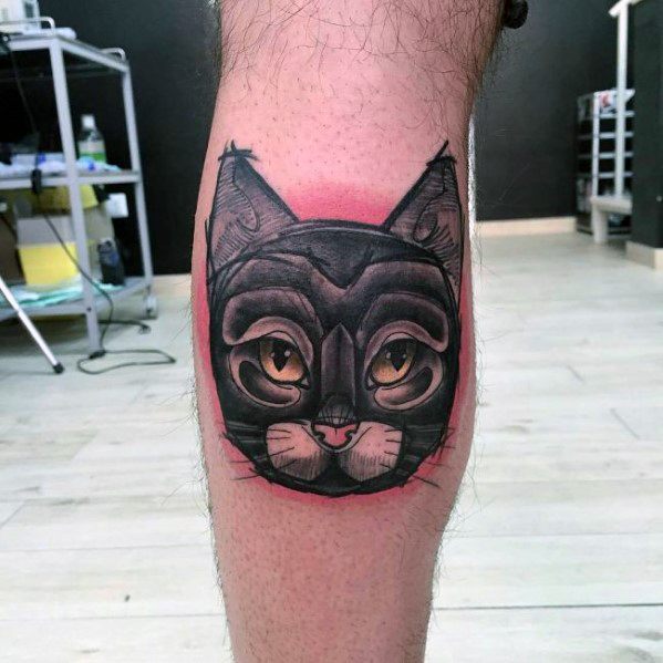 Bold neo-traditional cat tattoo on the leg, featuring a stylized mask-like design with vibrant shading and striking eyes.