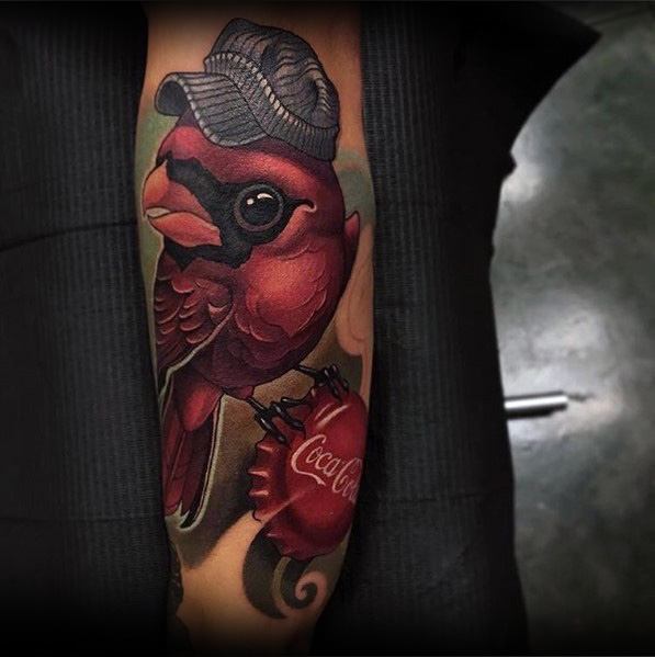 Creative Coca-Cola tattoo featuring a red cardinal wearing a cap, holding a bottle cap, with bold colors and fine details for a unique design.