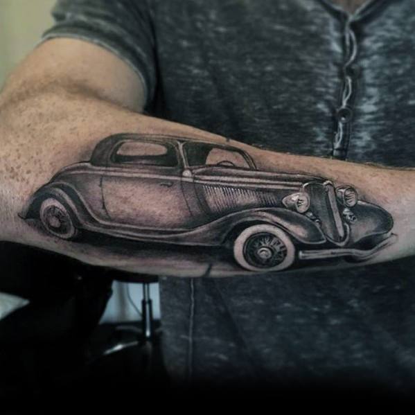 Realistic black and grey vintage Ford coupe tattoo on forearm, featuring intricate shading and fine details for a classic automotive design.