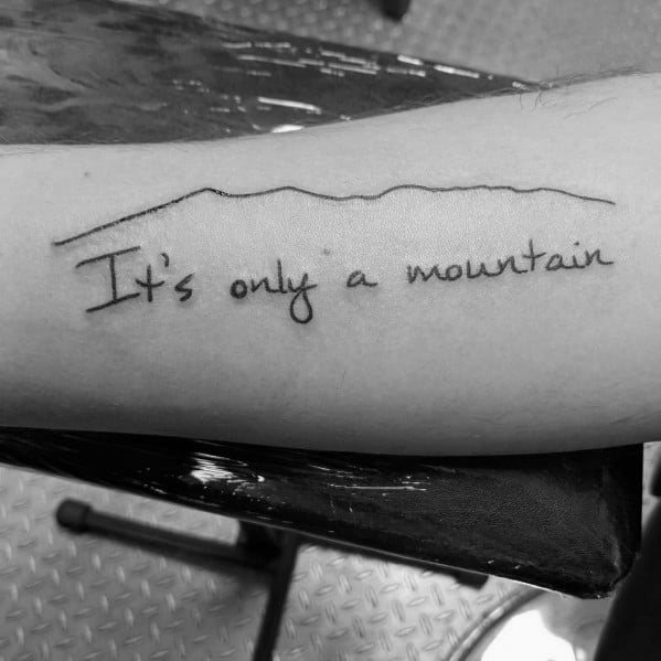 Minimalist tattoo with a simple mountain outline and the phrase 'It's only a mountain,' symbolizing perseverance and overcoming challenges.