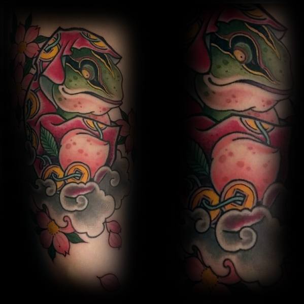 Japanese-style tattoo featuring a vibrant green and pink frog surrounded by gold coins, cherry blossoms, and swirling clouds, symbolizing prosperity and luck.
