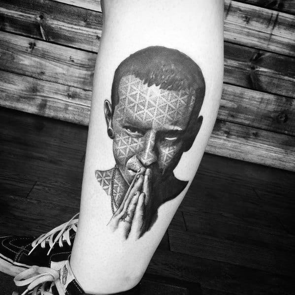 Black and gray tattoo of Chester Bennington with geometric pattern overlay, blending realism with abstract design on the leg.