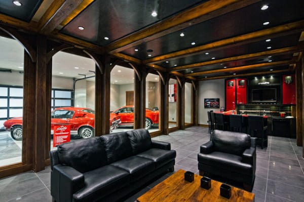 Luxury room with black leather seating, wooden accents, and a garage showcasing sleek red sports cars