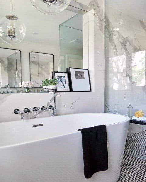 Freestanding tub with marble tile walls, black and white patterned floor, and pendant lights.