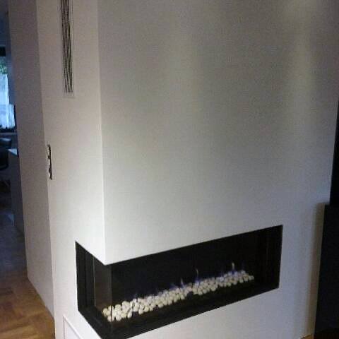 Modern minimalist corner fireplace with glass panels and decorative white stones.