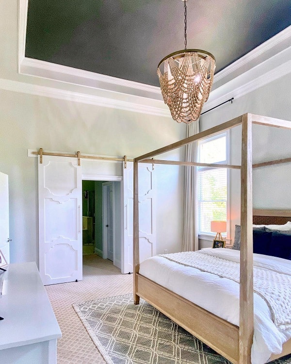 White sliding barn doors in a bright, modern bedroom with a four-poster bed and statement chandelier.