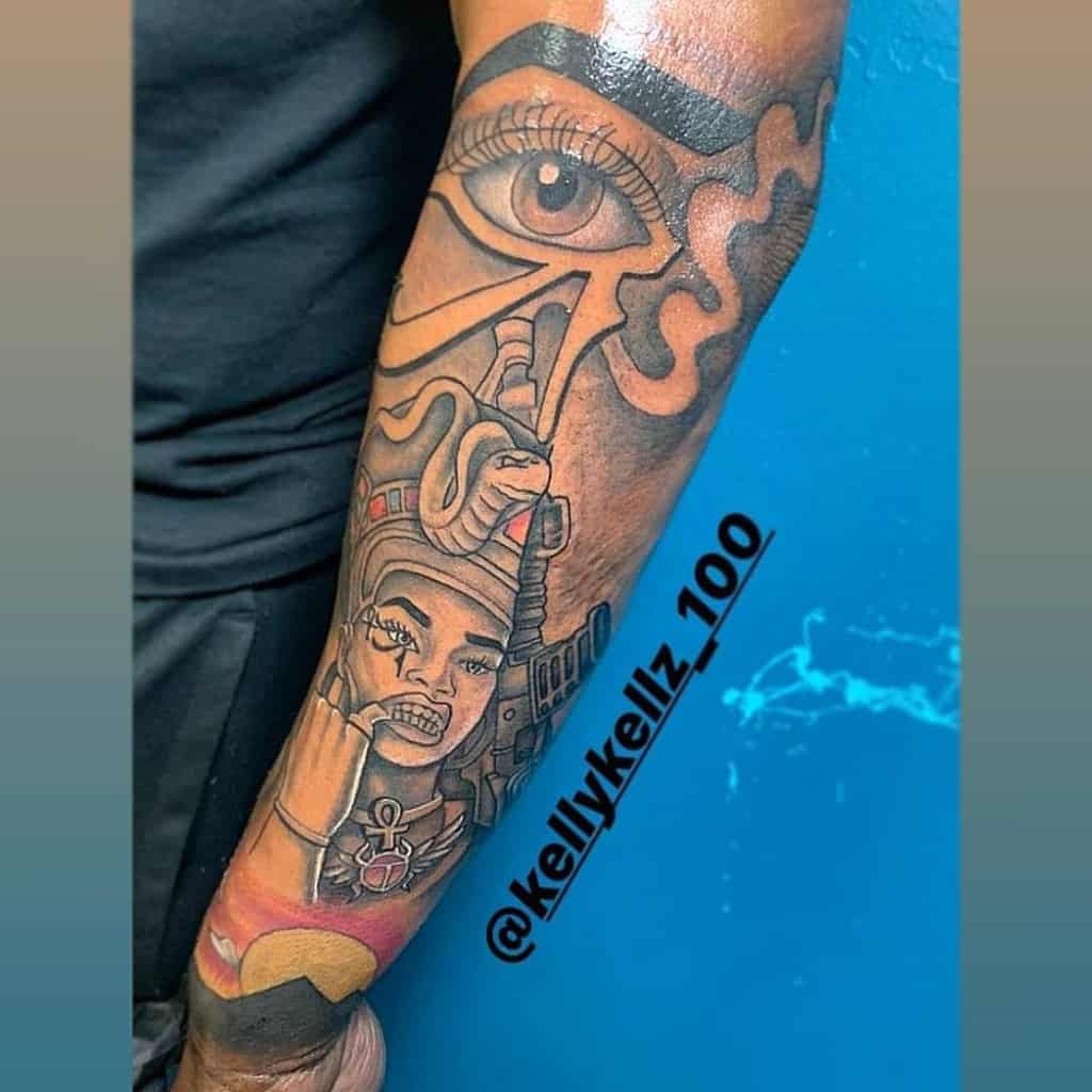Vibrant forearm tattoo combines modern artistry with ancient symbolism, featuring Queen Nefertiti adorned with a cobra and ankhs, complemented by the Eye of Horus for a powerful and dynamic design