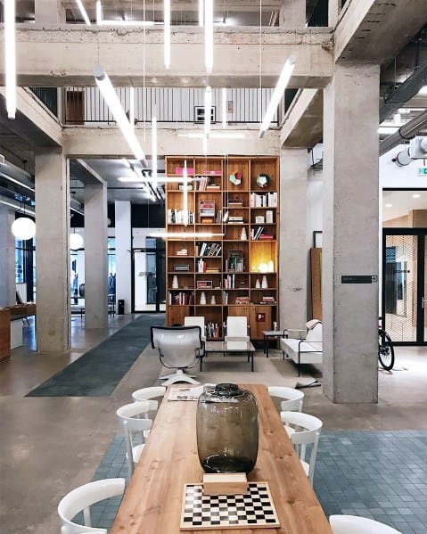 Modern office space with a long table, bookshelf, and stylish hanging lights