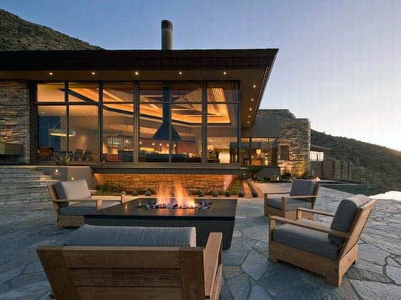 Modern house with large glass windows, outdoor seating area, and fire pit at dusk