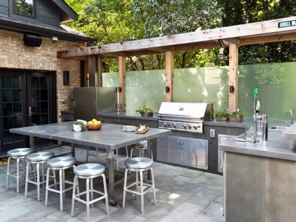 Outdoor kitchen featuring stainless steel appliances, barstools, a grill, and fruit under a wooden pergola