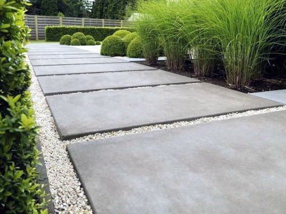 Concrete pavers with gravel accents, bordered by ornamental grasses and manicured shrubs.