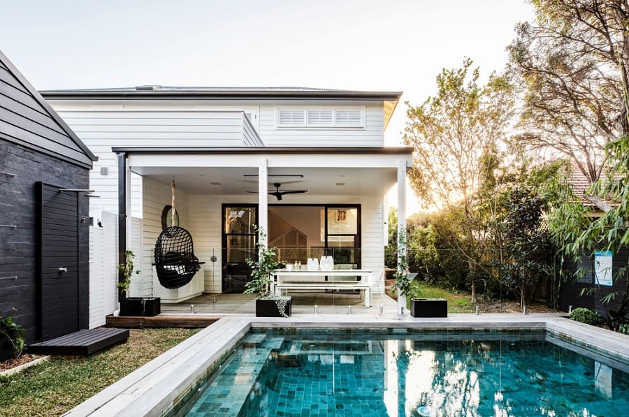 Modern backyard with a pool, outdoor shower, dining area, and hanging chair under a covered patio.