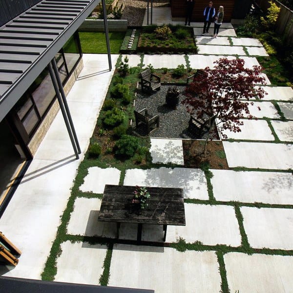 Chic patio with geometric concrete slabs, a wooden table, cozy chairs around a fire pit, and a charming small tree
