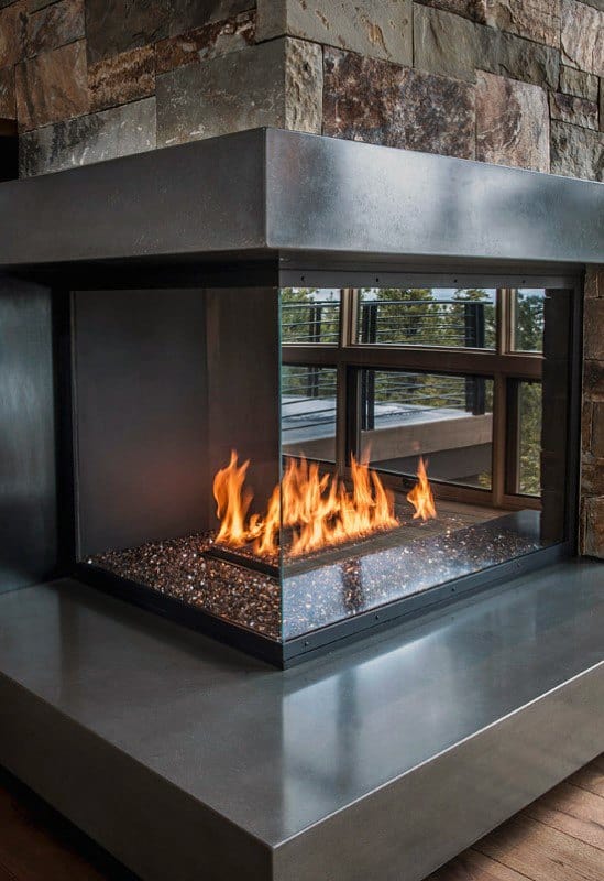 Contemporary glass corner fireplace with polished concrete base and stone wall backdrop.