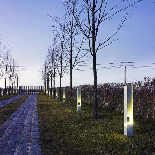 Stylish driveway lined with modern LED-lit posts, illuminating the cobblestone path and enhancing the surrounding trees at dusk
