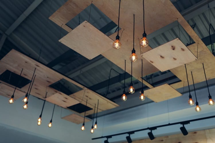 Industrial ceiling featuring exposed bulbs and wooden panels in a striking geometric arrangement