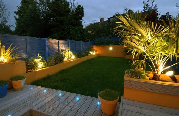 Yellow retaining walls with built-in planters, LED lighting, a wooden deck, and a lush lawn.