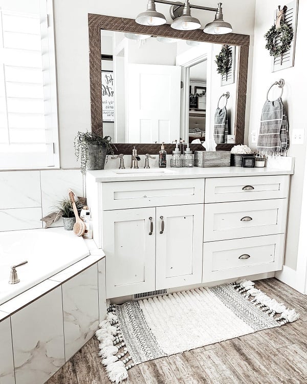 Farmhouse-style bathroom with large mirror, modern white vanity, and decorative rug on wooden floor, featuring natural accents and greenery