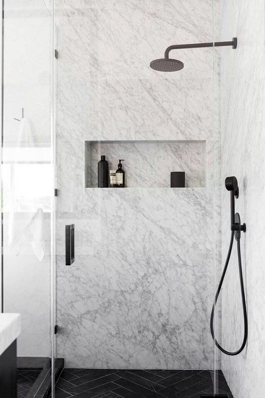 Minimalist shower with marble walls, black fixtures, and a recessed shelf for toiletries.