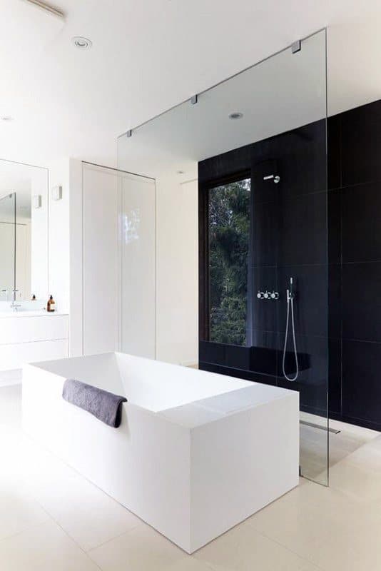 Modern bathroom with a freestanding white tub, glass shower partition, and black tiled wall.