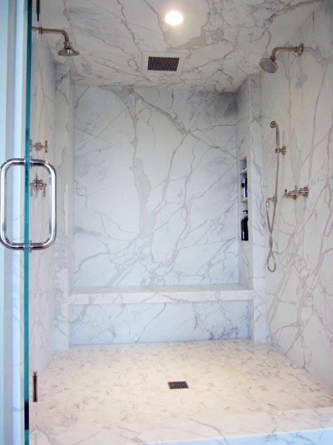 Spacious shower with white marble tiles, built-in bench, and dual showerheads.