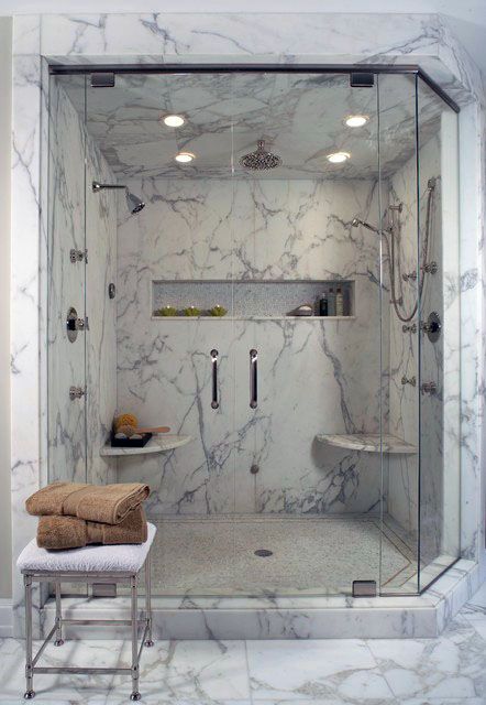 Luxury shower with marble walls, built-in bench, recessed shelf, and glass enclosure.