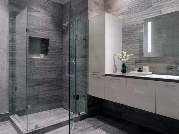 Modern bathroom with glass shower, gray textured tiles, floating vanity, and illuminated mirror.