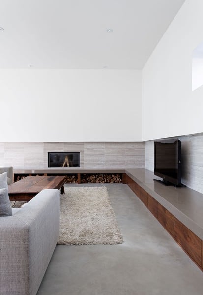 Minimalist living room with gray sofa, wood accents, a flat-screen TV, and a fireplace surrounded by logs