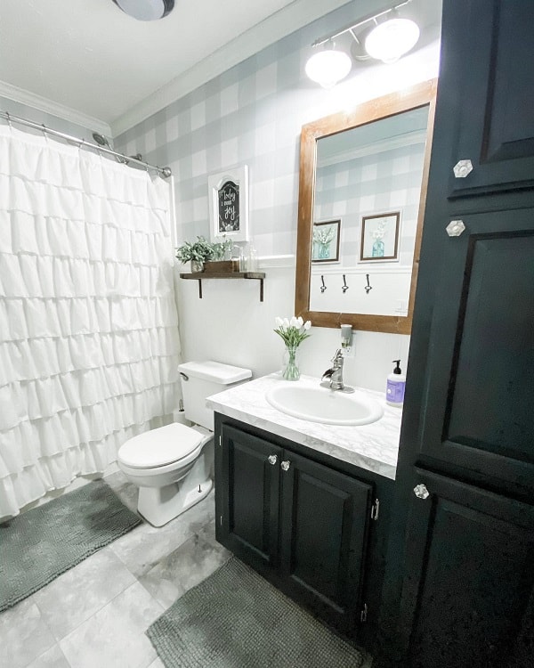 A bright farmhouse bathroom with a shower curtain, dark cabinets, and a vase of tulips on the countertop