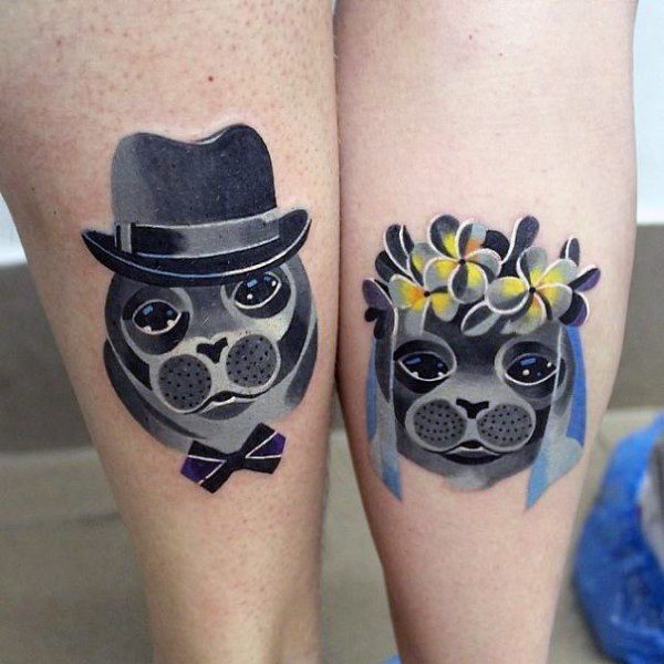 Matching calf tattoos of cartoon-style seals dressed as a groom and bride, symbolizing a playful, loving, and committed relationship.