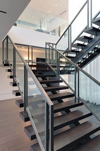 Modern interior featuring a sleek staircase of black metal and glass, leading to a sunlit upper floor