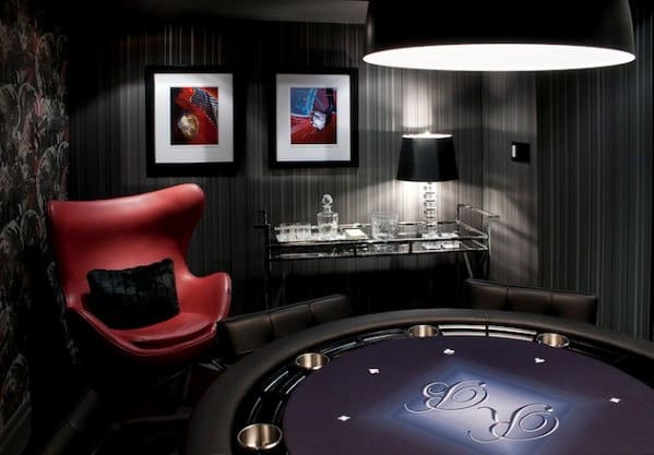 Sleek poker room with a round table, red chair, bar cart, and framed art on dark striped walls