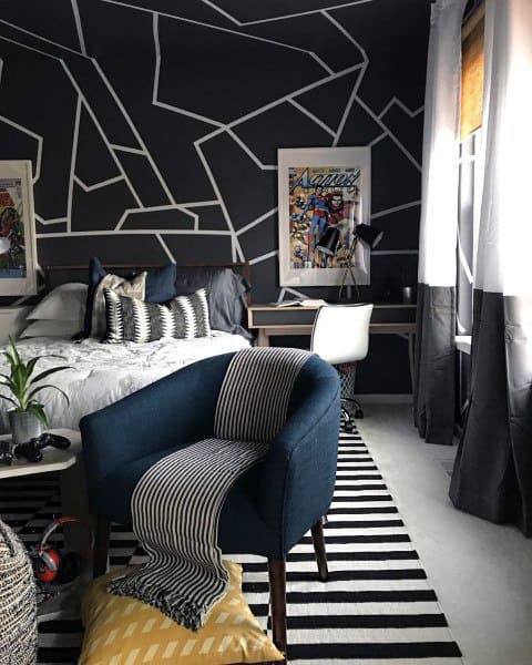 Modern teen boy bedroom with geometric black walls, blue chair, and comic art.