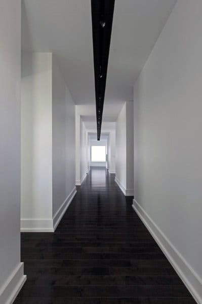 Long hallway with white walls, dark wood floors, and minimal white baseboard trim.