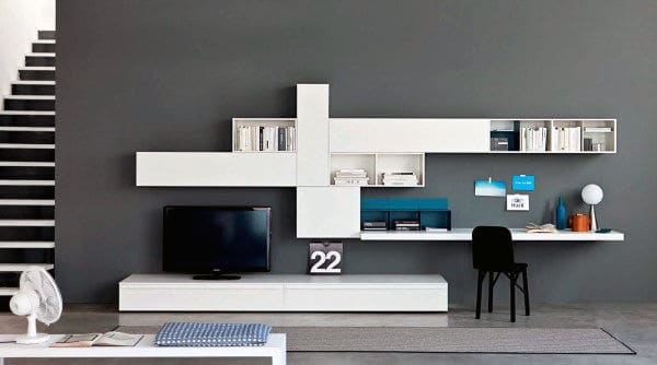 Modern living room with white modular shelves, a TV, desk with chair, and staircase on the left
